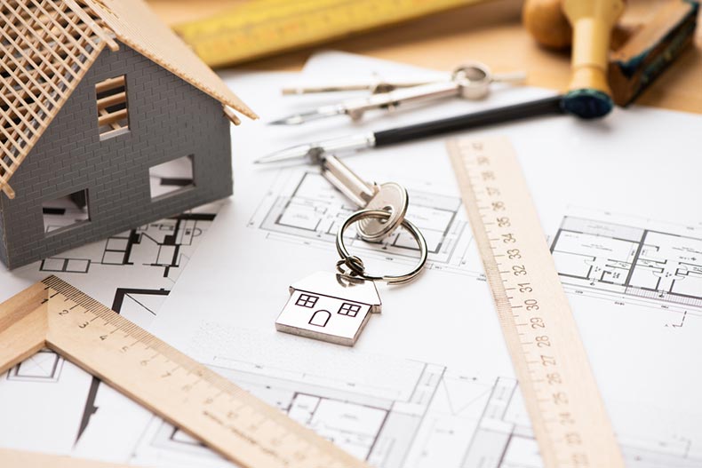 A model home beside a key on top of blueprints