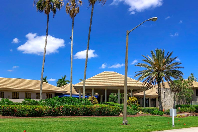 Exterior view of a clubhouse surrounded by bushes, palm trees, and a streetlight, located in the Boca Lago community of Boca Raton, Florida
