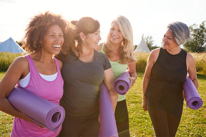 A group of female friends smiling and walking along a path with yoga mats