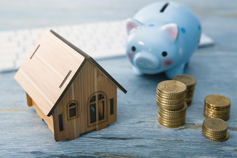 A small wooden house beside coins and a blue piggy bank