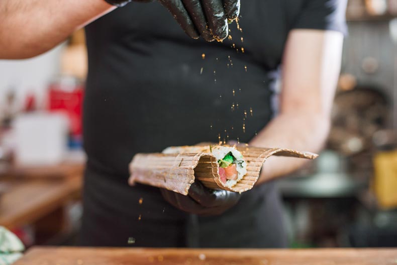 Close-up of professional chef's hands in black gloves making sushi and rolls in a restaurant kitchen