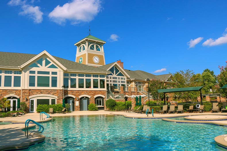 Exterior view of the clubhouse in Carolina Preserve against a blue sky with a resort-style pool in the foreground, located in Cary, North Carolina