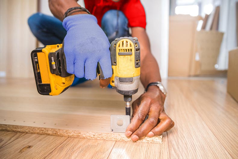 A carpenter drilling screws into a cupboard door on a home repair and renovation project