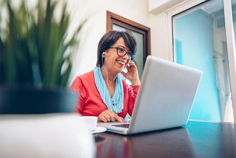 An older woman with earbuds in smiling while taking an online class