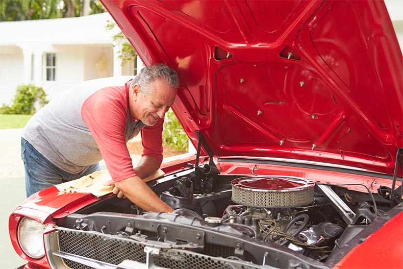 Retired man working on the engine of a classic car