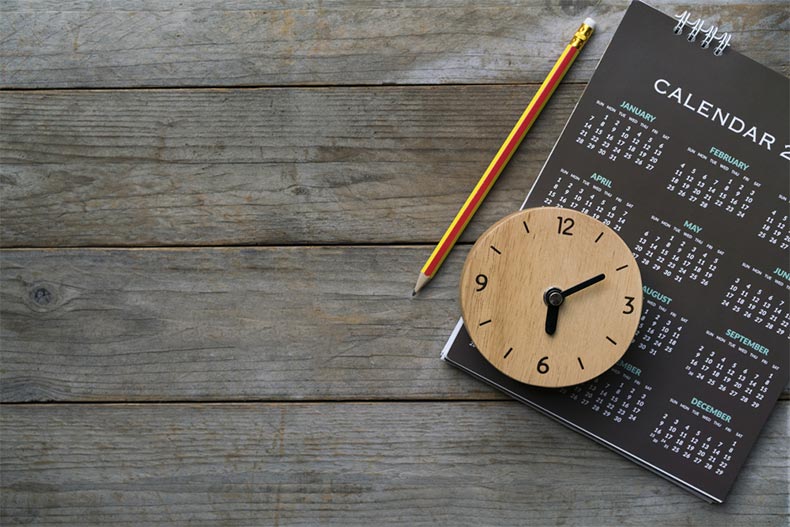 Close up of a clock, calendar, and pencil on a table