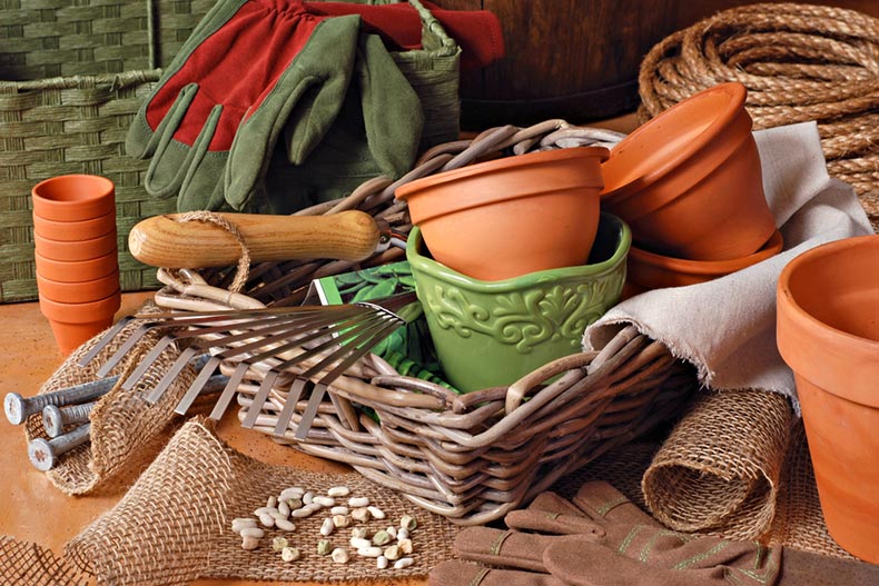 Flower pots, gardening tools, and planting supplies in a wicker basket with burlap and rope