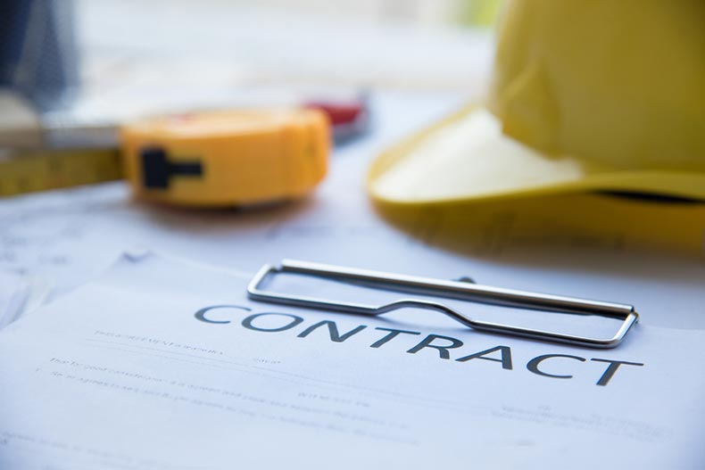 A hard hat and tape measure on a clipboard with a contract