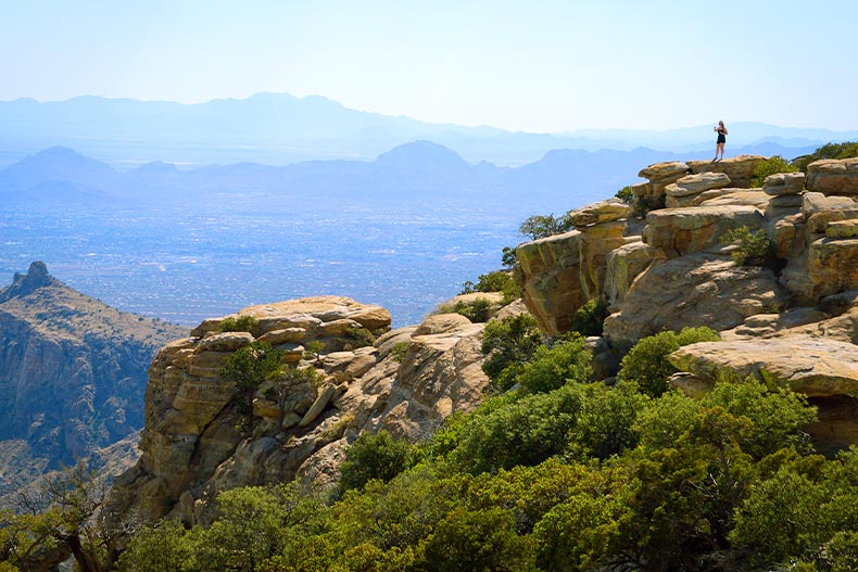 View of a mountain top with greenery in Coronado National Forest of Arizona. A lone hiker stands at the peak.