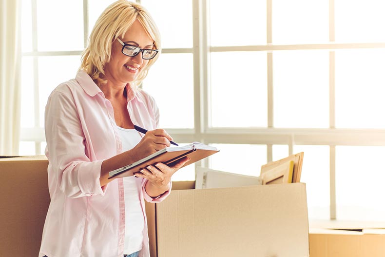 An older woman writing down notes as she packs moving boxes