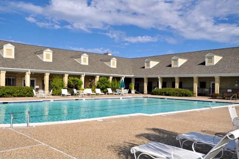 View of the outdoor pool and patio at CountryPlace on a sunny day with the clubhouse in the background.