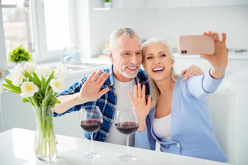 An older couple drinking wine and waving at a smart phone screen