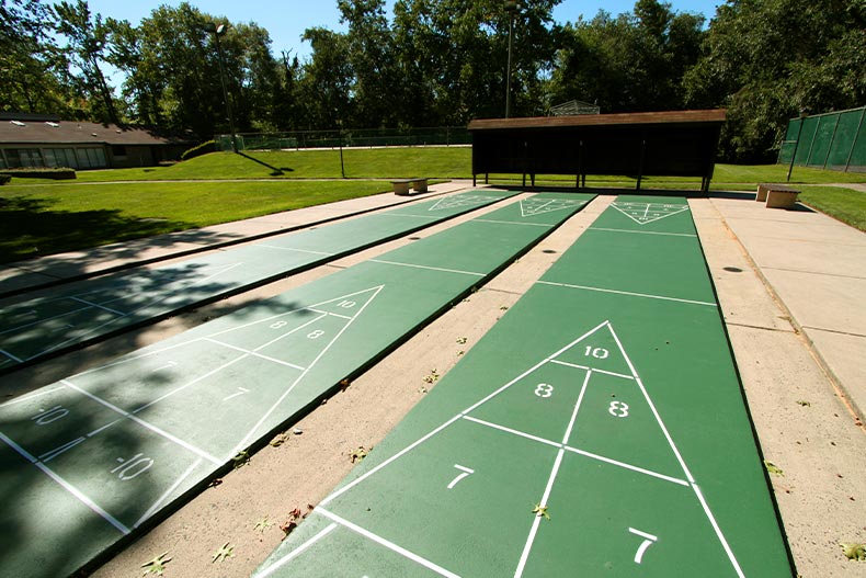 Three green shuffleboard courts leading to a brown covered scoreboard, located in Covered Bridge in Manalapan, New Jersey