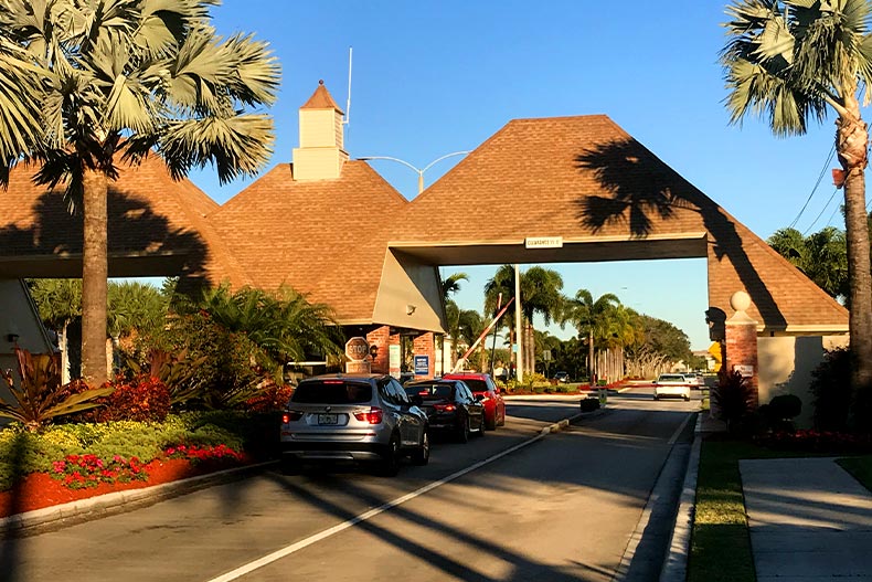Cars lined up at the gate house entrance for Century Village at Boca Raton, Florida along a street lined with palm trees and red flowers