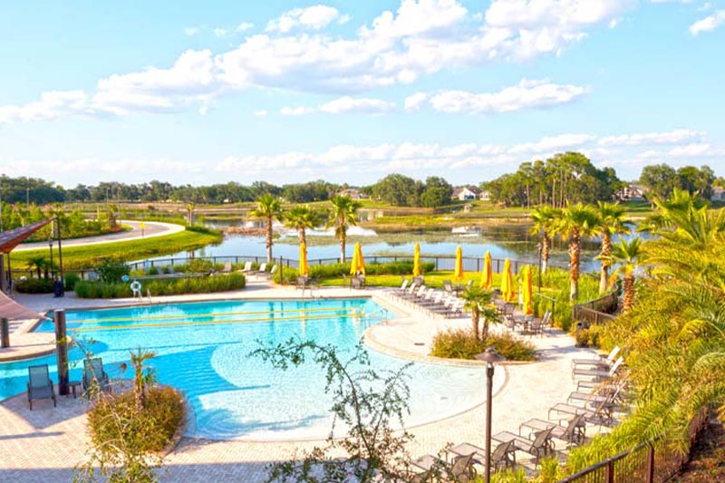 Aerial view of the outdoor pool and patio at Del Webb Orlando with a community lake and homes in the background.
