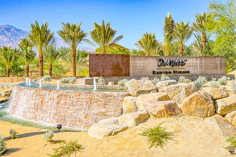 Palm trees and a water feature surrounding the community sign for Del Webb Rancho Mirage