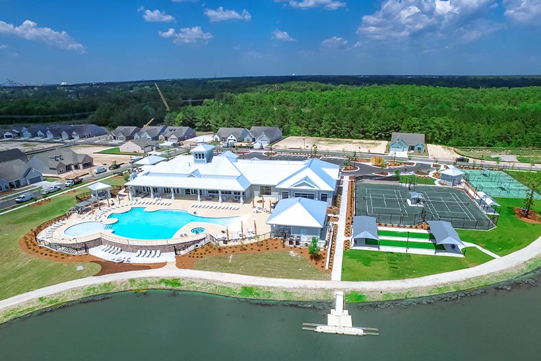 Aeriel view of the amenity center in Del Webb Wilmington, North Carolina including a clubhouse, pool, and athletic courts, surrounded by a forest, bay, and houses