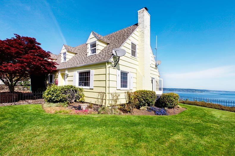 A red maple tree beside a small, yellow house with a view of the water