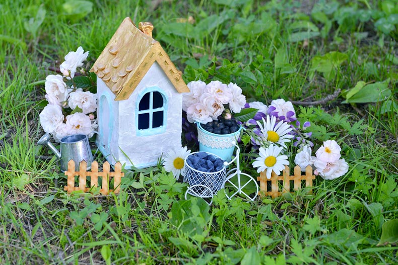 A tiny ceramic house on the grass with small flowers surrounding it