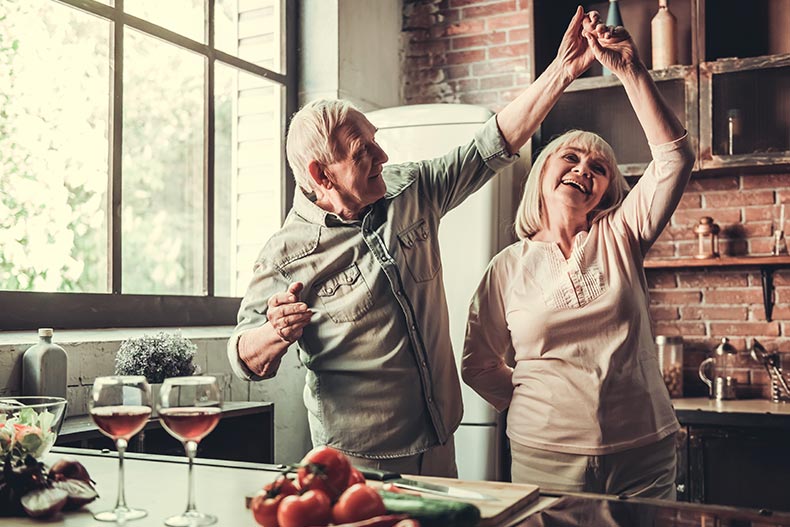 Happy senior couple dancing and smiling while cooking together in kitchen