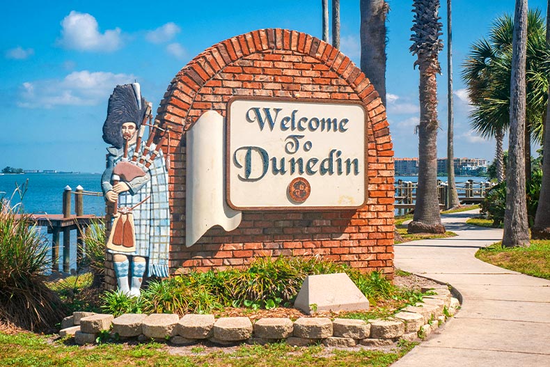 Photo of a welcome sign and a stone portrait of a man playing bagpipes in Dunedin, Florida