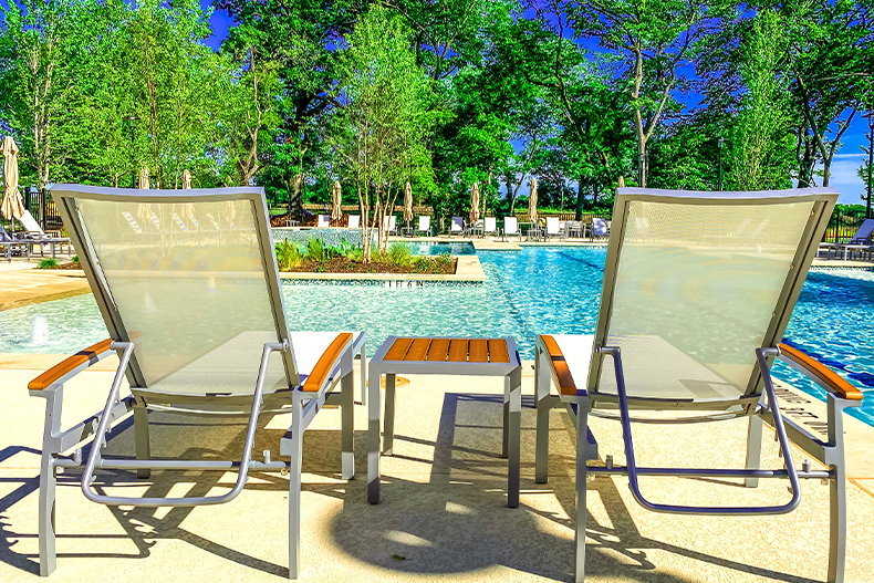 View of a resort-style pool and green trees from behind two pool chairs, located in Del Webb at Trinity Falls in McKinney, Texas