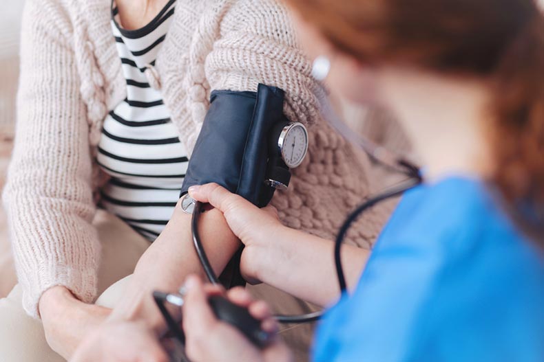 A nurse using a blood pressure sleeve to check a retired woman's vitals