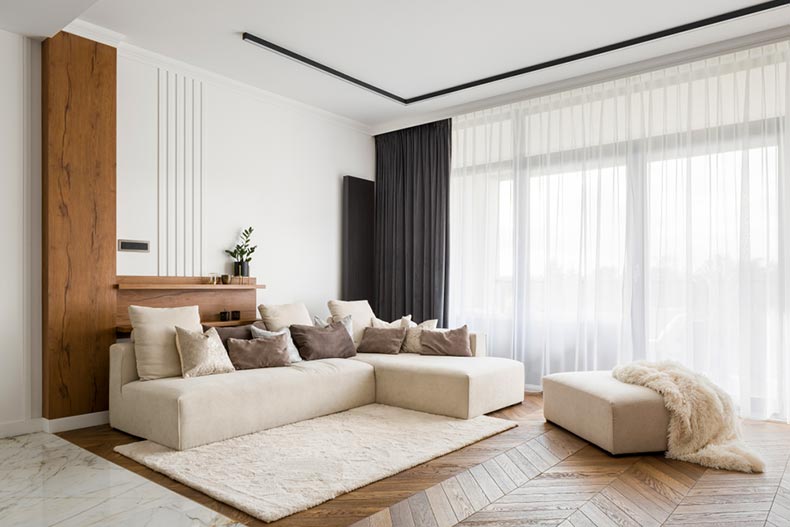 An elegant living room with a big sofa, a wooden floor, and big windows