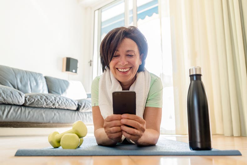 An older woman exercising in her home with a yoga mat, weights, and a water bottle