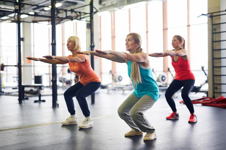 A group of mature women squatting and stretching arms forwards during a workout in a fitness center