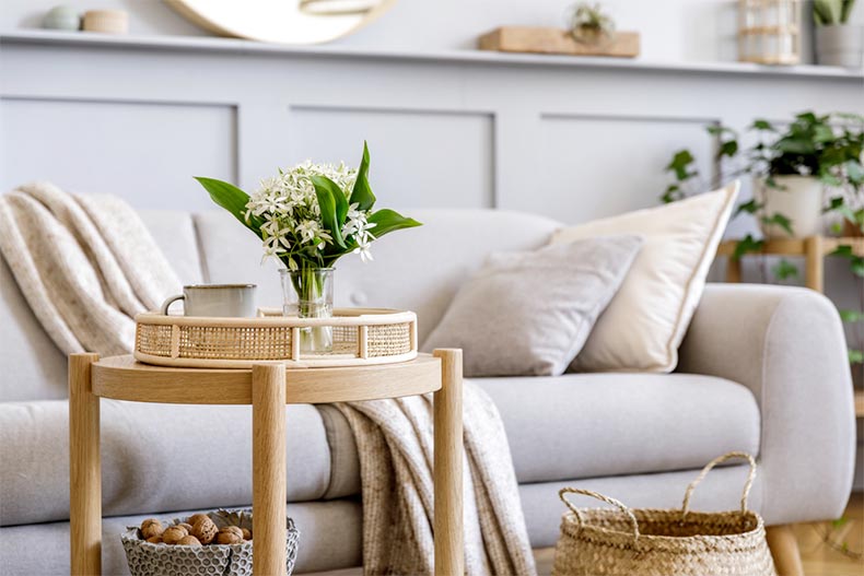 A living room with a sofa, a wooden coffee table, spring flowers in vase, and elegant personal accessories