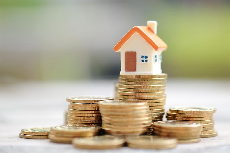 A small, ceramic house on top of a pile of coins to symbolize hoa fees