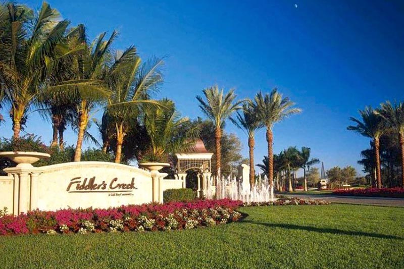 View of the community sign at Fiddler's Creek with landscaping and palm trees surrounding it.
