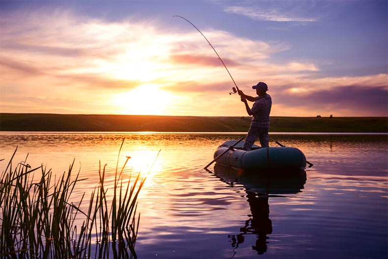 Older man fishing on boat during sunset
