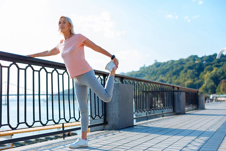 Older, athletic woman pausing to stretch her leg while running across a bridge