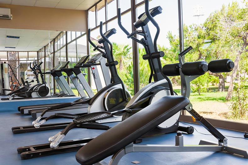 A fitness center with aerobic machines facing large windows
