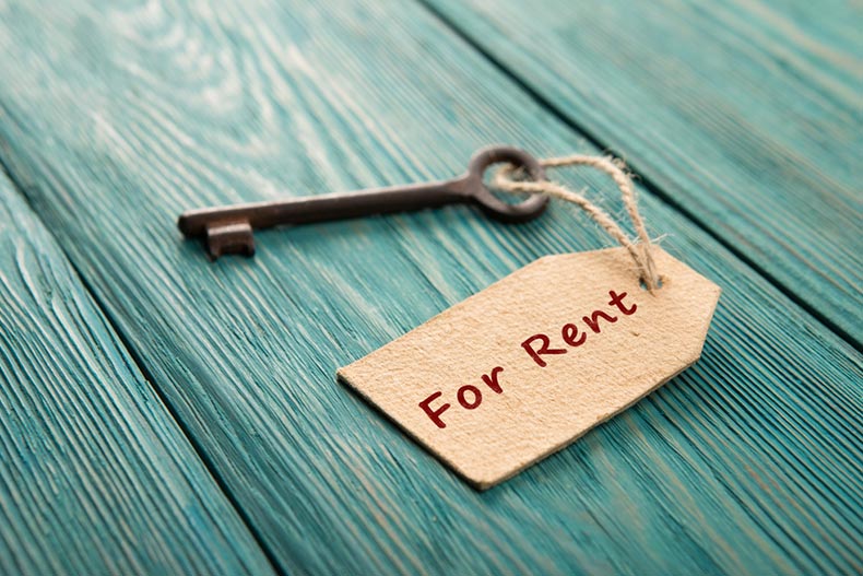 An old key with a "For Rent" tag on a blue wooden background