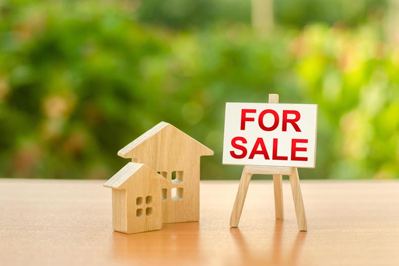 Two small wooden houses and a sign with the words "For Sale" on a table