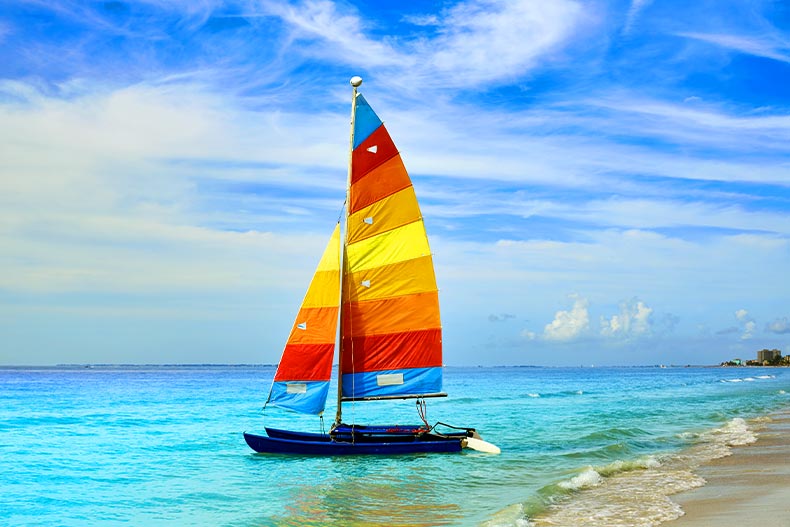  A sailboat with with an blue, red, orange, and yellow sail near the shore on the Gulf coast of Fort Myers, Florida