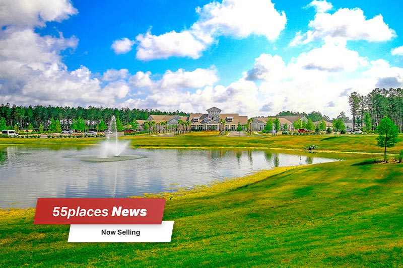 "55places News: Now Selling" banner over a picturesque pond in front of the clubhouse at Four Seasons at The Lakes of Cane Bay in Summerville, South Carolina