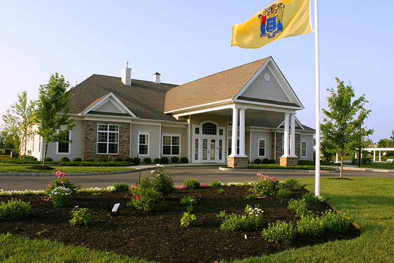 Exterior photo of the clubhouse in Four Seasons at Millville with a garden and the New Jersey state flag in front