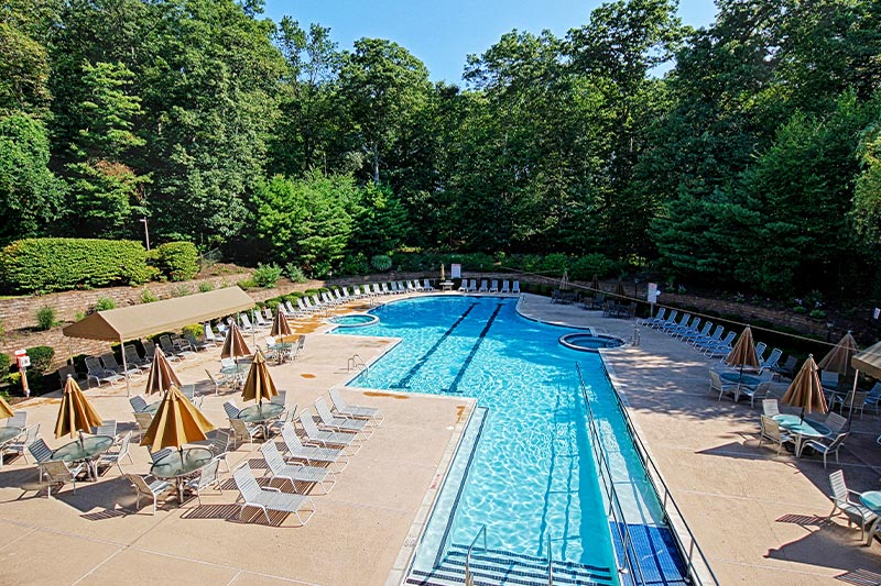Aerial view of the outdoor pool and patio at Fox Hills with a forested area in the background. 