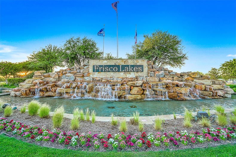 Flags, a water feature, and plants surrounding the community sign at Frisco Lakes in Frisco, Texas