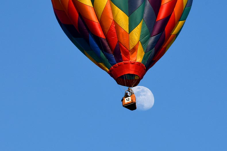 Worms-eye view of a rainbow hot air balloon against a daytime moon located in Fuquay-Varina, North Carolina