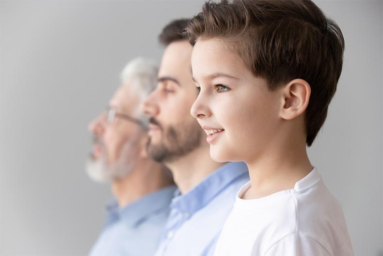 A young boy looking forward as he stands in a row with his father and grandfather