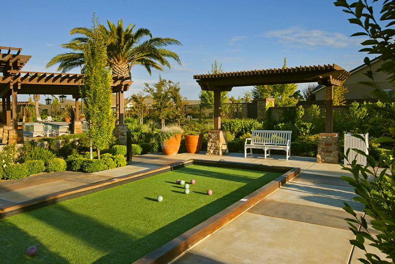 A bocce ball court with colorful game balls in place for a game surrounded by shrubbery and a shaded seating area, located in Glenbrooke in Elk Grove, California