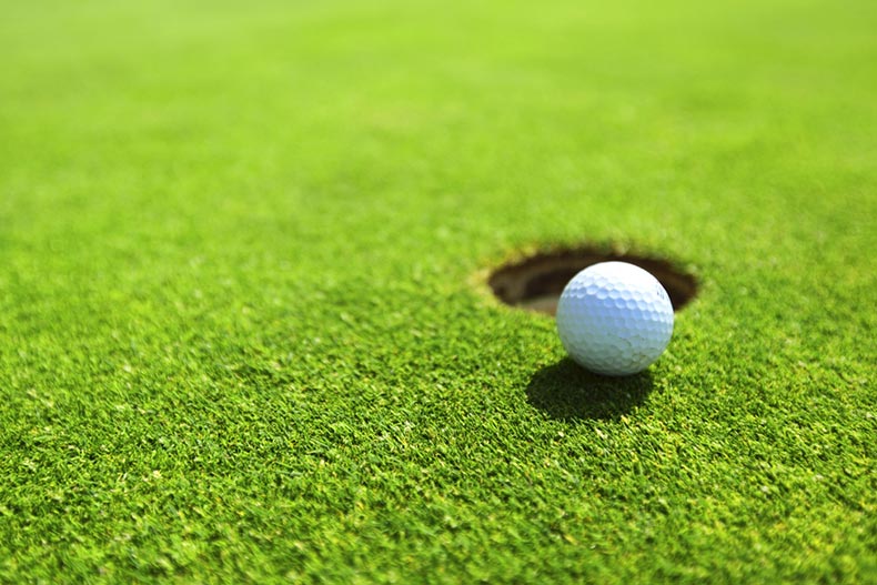 A golf ball on the lip of cup on a golf course