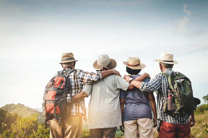 A group of older adults with their backs to the camera linking arms and looking towards the sunset