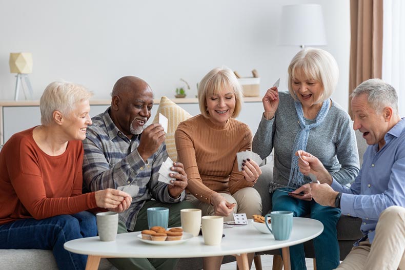 Happy senior friends sitting on couch and playing cards while drinking tea