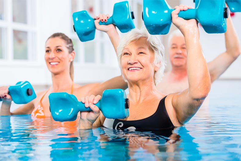 Young and older people in a pool doing water gymnastics with dumbbells